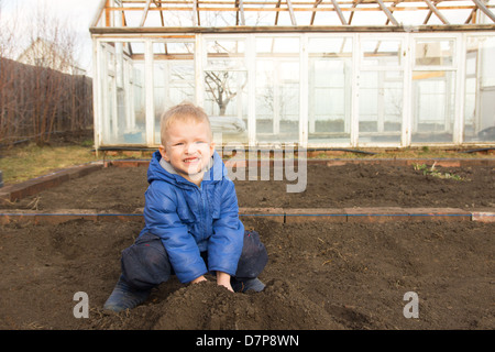 Happy smiling joyeuse enfant (garçon) de creuser le sol, travaillant dans la région de Spring Garden Village. Peu d'agriculteurs. Banque D'Images