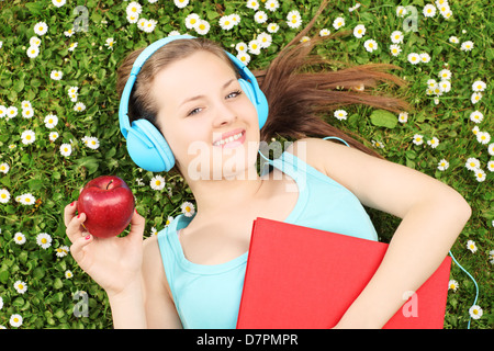 Jeune femme à l'écoute de la musique et tenant une pomme, sur une herbe verte avec daisies Banque D'Images