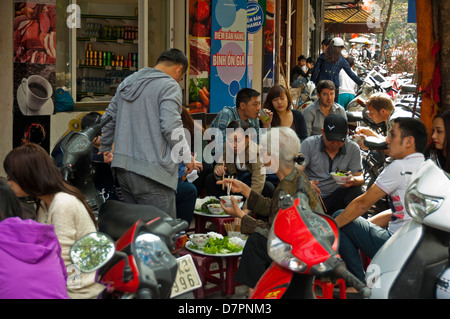 Vue horizontale de gens assis dans la rue Pho traditionnel de l'alimentation, les nouilles, sur la chaussée à Hanoi. Banque D'Images