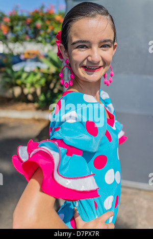 Un enfant dans son danseur hispanique de l'adolescence tôt pose dans son costume de danse flamenco traditionnel coloré, robe, boucles d'oreilles et d'un sèche avant. Banque D'Images