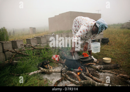 Une femme africaine cuisiniers à l'extérieur sur un feu de bois comme la brume en rouleaux Banque D'Images