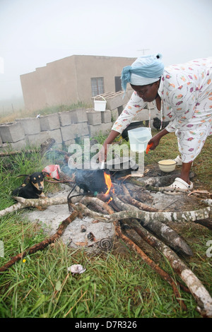 Une femme africaine cuisiniers à l'extérieur sur un feu de bois comme la brume. Banque D'Images