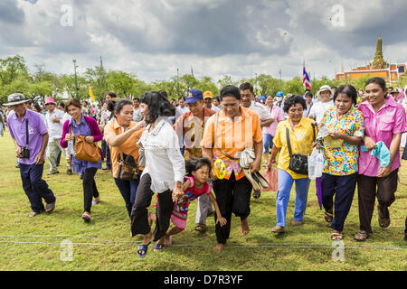 Bangkok, Thaïlande. 13 mai, 2013. Voyages d'un enfant et est traîné par sa mère car les gens se précipiter sur Sanam Luang pour recueillir la bénédiction des semences de riz, après la cérémonie du Labour Royal. Après la cérémonie, des milliers de Thaïlandais, le plus souvent la famille formers, Rush sur le sol labouré pour ramasser le riz béni les graines semées par les prêtres brahmanes. La cérémonie du Labour Royal est tenue en Thaïlande pour marquer le début de la saison de culture du riz. La date est généralement en mai, mais est déterminé par les astrologues de la cour et varient d'année en année. Au cours de la cérémonie, deux boeufs sacrés sont attelés à une charrue en bois Banque D'Images