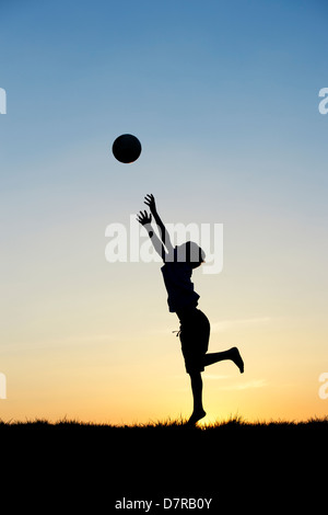 Garçon jouant avec un foot au coucher du soleil. Silhouette Banque D'Images