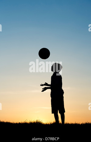 Garçon jouant avec un foot au coucher du soleil. Silhouette Banque D'Images