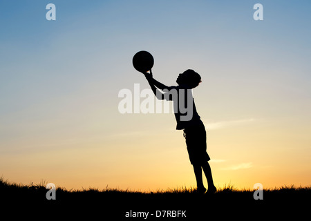 Garçon jouant avec un foot au coucher du soleil. Silhouette Banque D'Images