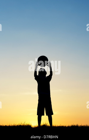 Garçon jouant avec un foot au coucher du soleil. Silhouette Banque D'Images