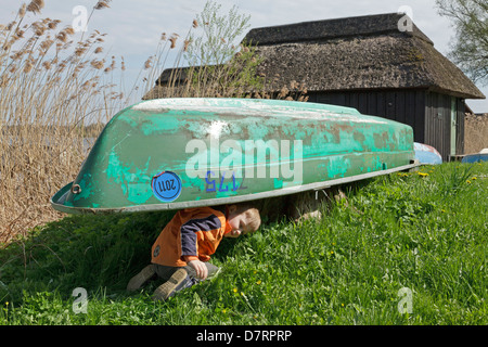 Jeune garçon se cachant sous un hangar à bateau, au bord de l'eau, Schaalsee Lenschow, Schleswig-Holstein, Allemagne Banque D'Images