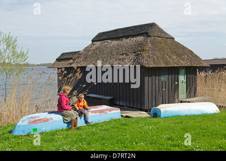 Mère et fils se reposant à côté d'un garage à bateaux au bord de l'eau, Schaalsee Lenschow, Schleswig-Holstein, Allemagne Banque D'Images