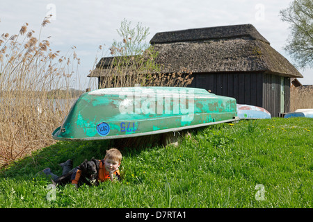 Jeune garçon à côté d'un bateau, d'un hangar à bateaux au bord de l'eau, Schaalsee Lenschow, Schleswig-Holstein, Allemagne Banque D'Images