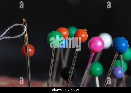 Une aiguille filetée et broches tête de bille dans un pin cushion contre un fond sombre Banque D'Images