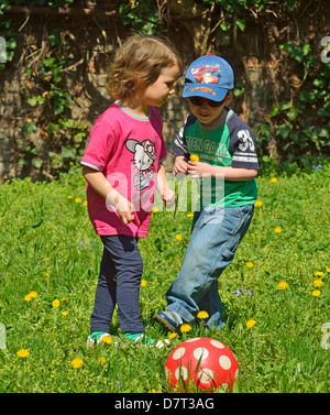 4 ans, petit garçon et fille jouant sur l'arrière-cour avec une boule rouge à l'extérieur Banque D'Images