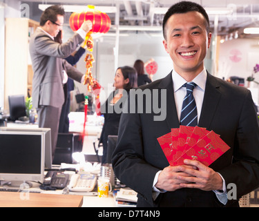 Businessman holding enveloppes rouges et ses collègues pendaison décorations pour le nouvel an chinois Banque D'Images