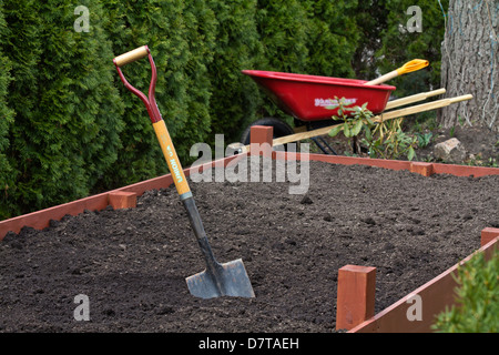 Une bêche dans un sol dans un lit surélevé vide dans le jardin avec brouette Spring fonctionne au-dessus de personne horizontale aux États-Unis haute résolution Banque D'Images