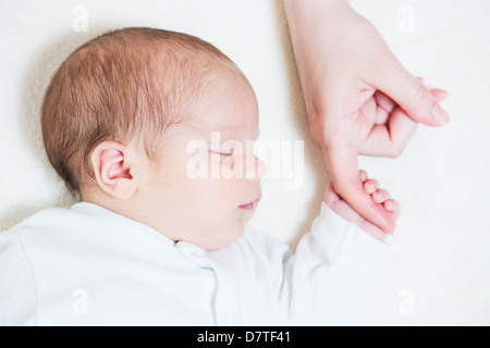 Mignon bébé de un mois du doigt de maintien de sa mère pendant le sommeil Banque D'Images