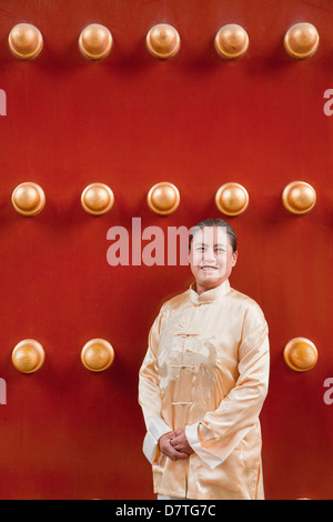 Femme mature en vêtements traditionnels debout à côté de la porte traditionnelle chinoise Banque D'Images