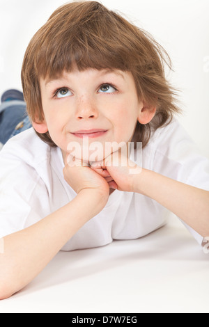 Fond blanc photographie de jeunes heureux garçon enfant fixant, en appui sur les mains, jusqu'à la pensée et Banque D'Images