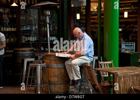 Man reading newspaper et prendre un verre, Borough Market, London, England Banque D'Images