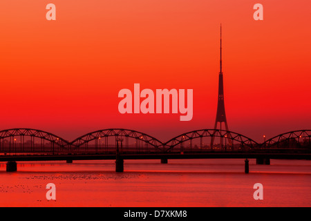 Tour de télévision et de radio de Riga avec le célèbre pont de chemin de fer au coucher du soleil Banque D'Images