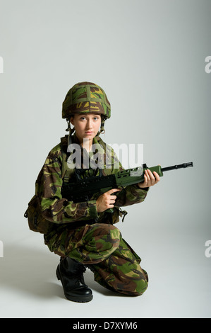 Femme Soldat portant des uniformes de camouflage militaire britannique et la tenue d'une SA80 carabine. Studio photo avec un fond uni. Banque D'Images