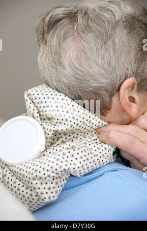 Femme âgée à l'aide d'une bouteille d'eau chaude pour le cou et la douleur de l'épaule Banque D'Images