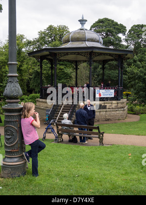 Jeune enfant /girl appuyé contre un lampadaire avec les personnes âgées et Buxtons Kiosque en arrière-plan le Derbyshire Banque D'Images