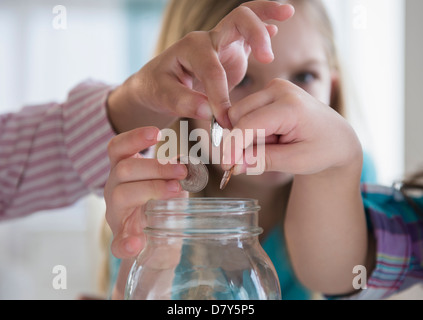 Girls putting coins in savings jar Banque D'Images