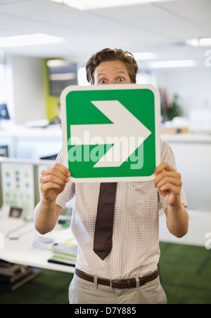 Businessman holding arrow sign in office Banque D'Images
