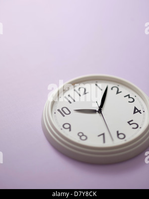 Une petite horloge murale sur un mur violet clair. Banque D'Images