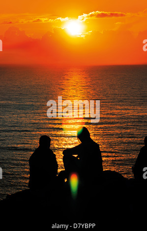 L'Espagne, Saint James Way : St Jacques pèlerins assis sur la falaise du Cap Fisterra regardant le coucher du soleil Banque D'Images