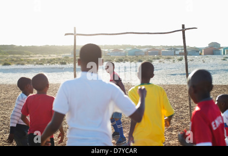 Boys playing soccer together in dirt field Banque D'Images