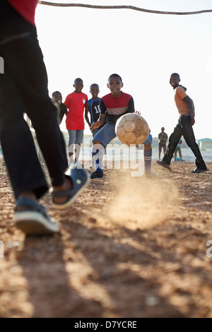 Boys playing soccer together in dirt field Banque D'Images