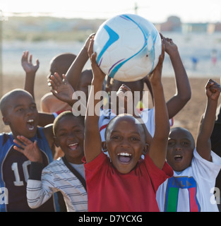 Boys playing soccer together in dirt field Banque D'Images