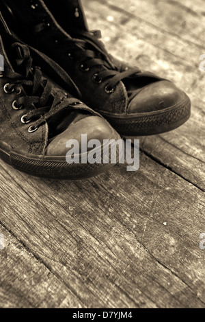 Les vieilles chaussures. Old black sneakers sur plancher en bois, image monochromatique. Banque D'Images