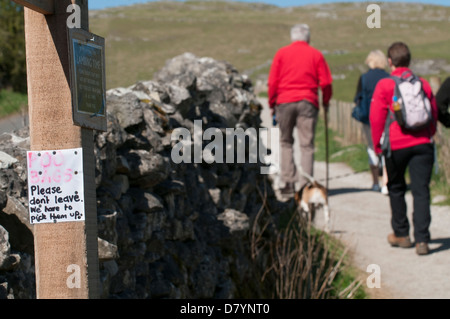 Close-up of note manuscrite jointe au poste en bois pour les propriétaires de chiens pour enlever la saleté poo  + dog walkers en fond - Malham, Yorkshire, UK Banque D'Images