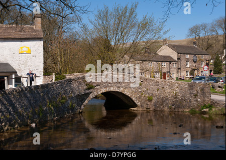 L'homme se distingue par la stone pont à travée unique au-dessus du centre de Malham Beck Dales pittoresque village sur sunny day - Malham, North Yorkshire, England, UK Banque D'Images