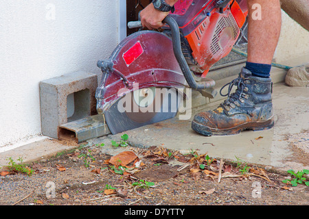 Workman avec une scie pour couper le béton humide Banque D'Images