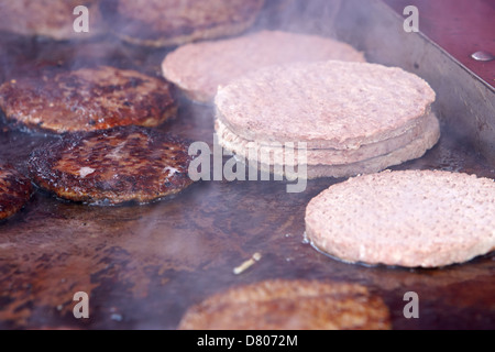 Hamburgers transformés crus et cuits sur une télévision commerciale grill à un événement en plein air Banque D'Images