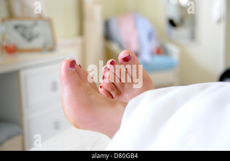 Les pieds avec les ongles des orteils peints en rouge qui dépasse de la fin du lit couché dans le matin Banque D'Images