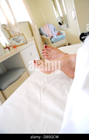 Les pieds avec les ongles des orteils peints en rouge qui dépasse de la fin du lit couché dans le matin Banque D'Images