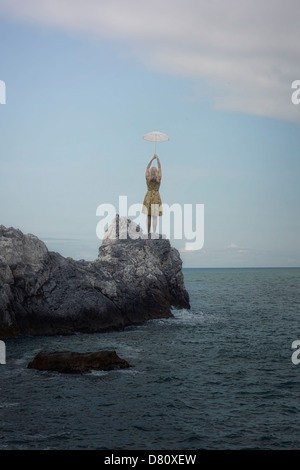 Une fille dans une robe jaune avec un parapluie sur une falaise dans la mer Banque D'Images