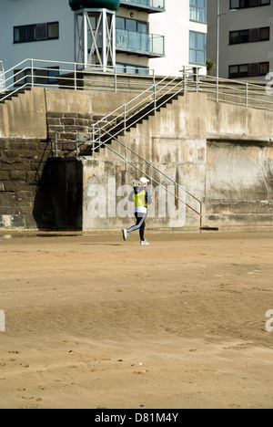 Woman running on beach, la baie de Swansea, Swansea, Pays de Galles du Sud. Banque D'Images