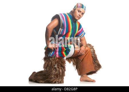 Un homme pose dans une position dynamique accroupie sur un fond blanc Uni. Il porte une tunique sans manches rayée multicolore vibrante avec ourlet frangé, un bandeau à motifs assorti et marron Banque D'Images