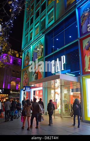 Les clients à l'extérieur du magasin de mode Gap magasinent avec la fenêtre avant Illuminations colorées sur Oxford Street West End de Londres, Angleterre ROYAUME-UNI Banque D'Images