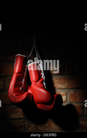 Gants de boxe rouge accroché sur un mur de briques dans une tache de lumière Banque D'Images