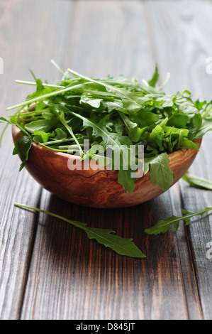 Feuilles de roquette fraîche dans bol en bois sur un fond de bois Banque D'Images