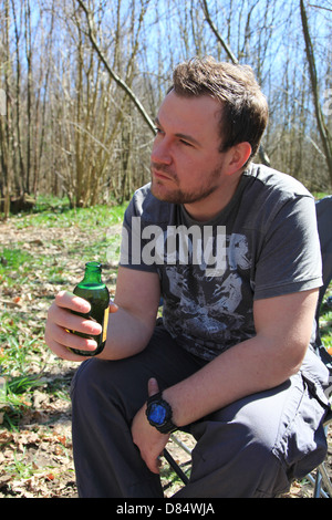 L'homme dans son début des années 30, la consommation de bière et à la fed up en camping dans les bois. Banque D'Images