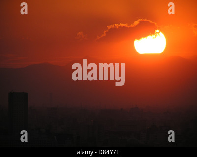 Un magnifique coucher de soleil sur Tokyo, Japon, capturé le 2 octobre 2003. La photo met en valeur la ligne d’horizon de la ville alors que le soleil se couche derrière ses imposants bâtiments, offrant une vue sur le paysage urbain dynamique avec un ciel coloré en toile de fond. Banque D'Images