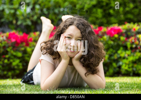 Photo horizontale de jeune fille couchée sur l'herbe avec des buissons à fleurs en arrière-plan sur une belle journée à l'extérieur Banque D'Images