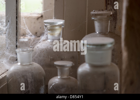 De vieilles bouteilles et contenants en verre recueillir la poussière et les toiles d'araignée dans le coin d'une vieille salle de stockage. Banque D'Images